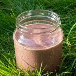 Healthy, vegan, berry smoothie being enjoyed in the garden for breakfast with grass backdrop.