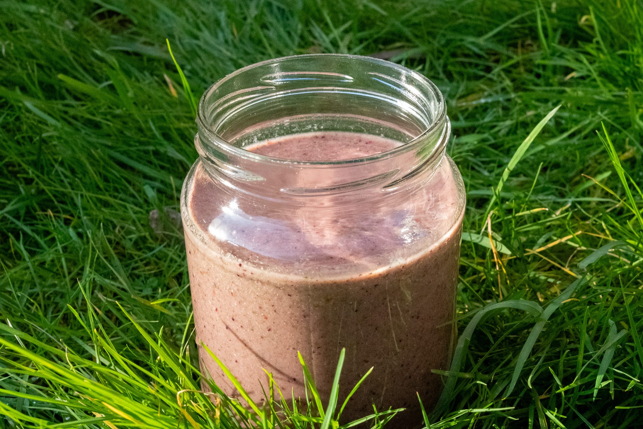 Healthy, vegan, berry smoothie being enjoyed in the garden for breakfast with grass backdrop.