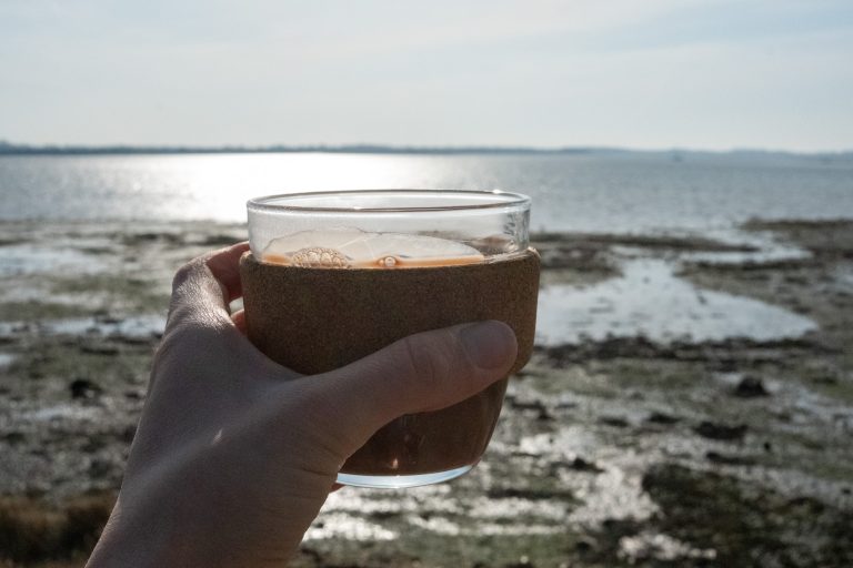 Healthy, vegan hot chocolate in a travel cup with the sea behind it.