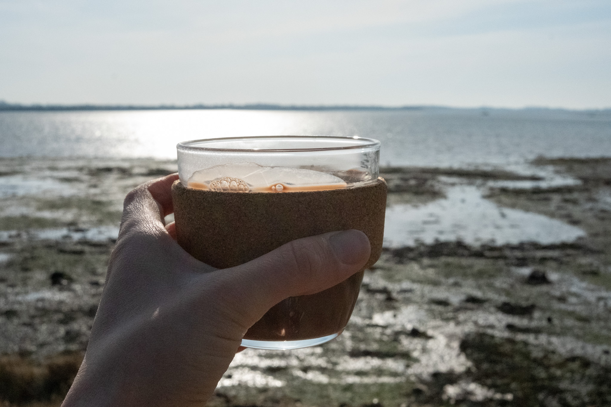 Healthy, vegan hot chocolate in a travel cup with the sea behind it.